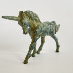 May include: A small, green bronze unicorn figurine. The unicorn is standing with its head lowered and its horn pointing forward.