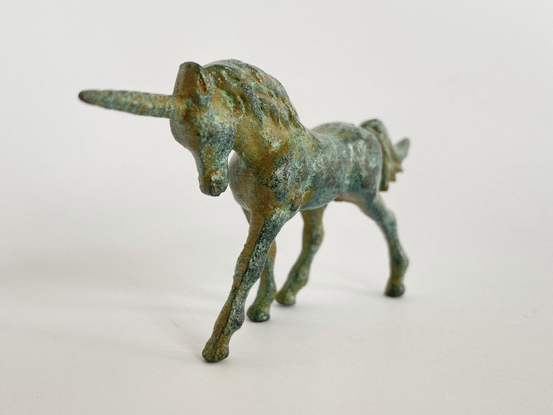 May include: A small, green bronze unicorn figurine. The unicorn is standing with its head lowered and its horn pointing forward.