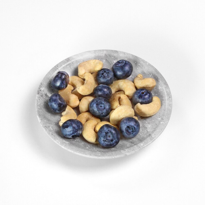 May include: A gray marble bowl filled with cashews and blueberries. The bowl is on a white background.