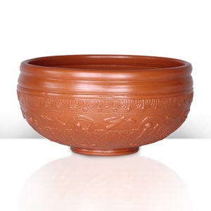 Op de afbeelding: Een terracotta kom met een decoratief ontwerp met gestileerde figuren en geometrische patronen. De kom heeft een brede rand en een ronde bodem.