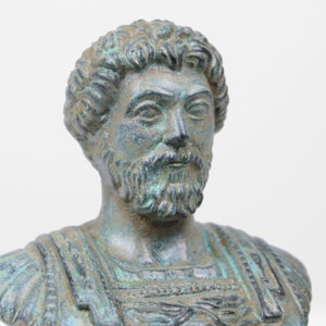 May include: A bronze bust of a man with a beard and short hair. The bust is weathered and has a green patina.