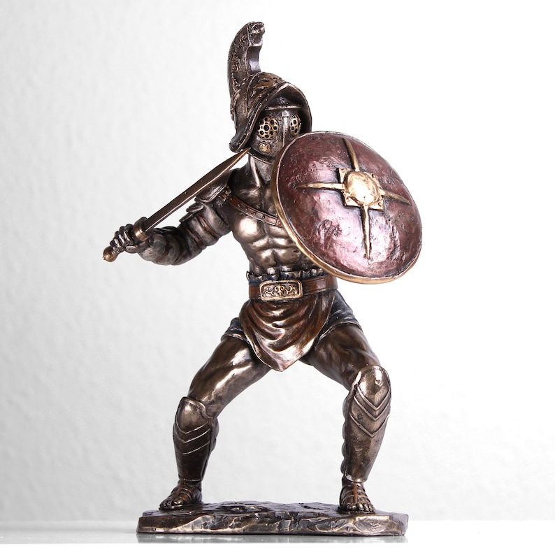 May include: Bronze statue of a gladiator holding a sword and shield. The gladiator is wearing a helmet and armor. The statue is on a base.