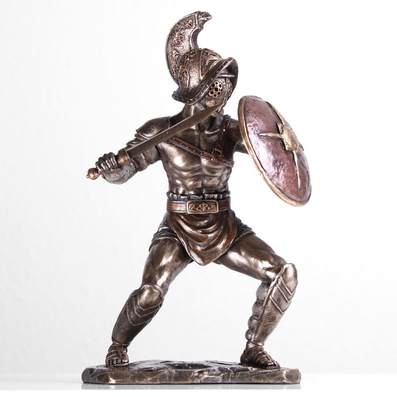 May include: Bronze statue of a gladiator holding a sword and shield. The gladiator is wearing a helmet and armor. The statue is standing on a rocky base.