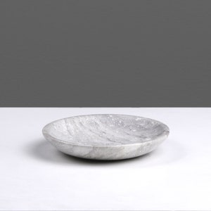 May include: A round, gray marble dish with a slightly rippled surface. The dish is empty and sitting on a white surface.