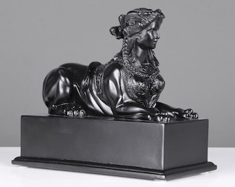 Könnte beinhalten: Schwarz-weiße Statue einer Frau mit einem Löwenkörper. Die Statue steht auf einem schwarzen Sockel.