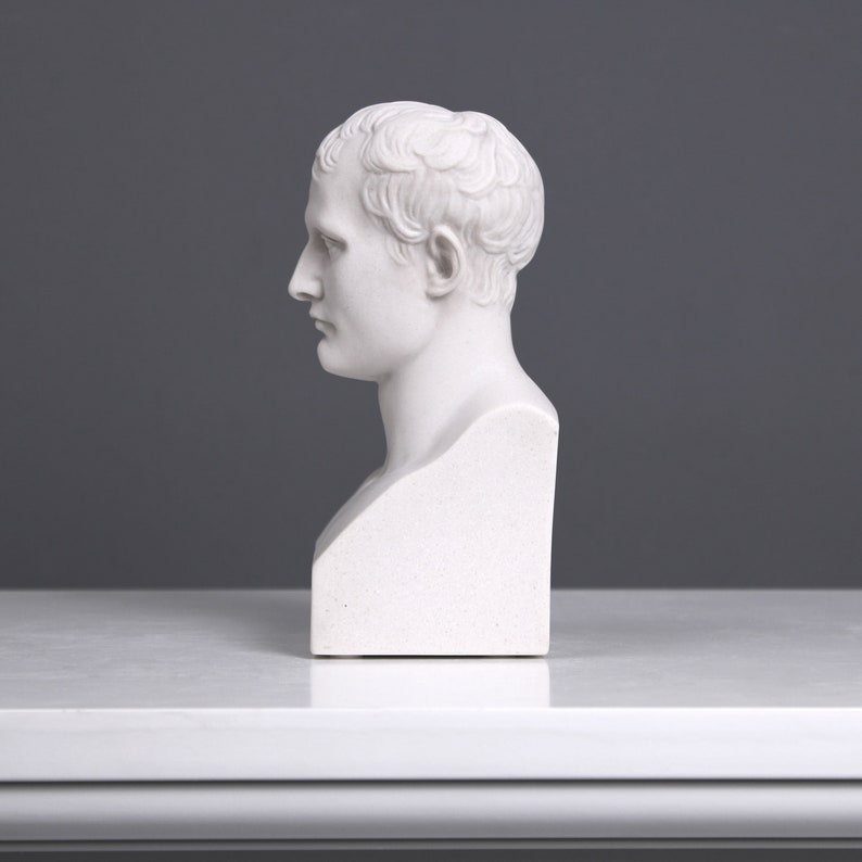 May include: White plaster bust sculpture of a man with short hair. The bust is on a white pedestal.