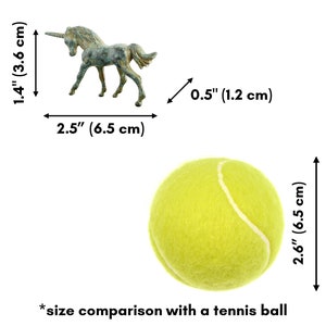 May include: A bronze unicorn figurine, approximately 3.6 cm tall and 6.5 cm long, next to a yellow tennis ball for size comparison. The unicorn is standing on all four legs with its head tilted slightly to the side. The tennis ball is 6.5 cm in diameter.