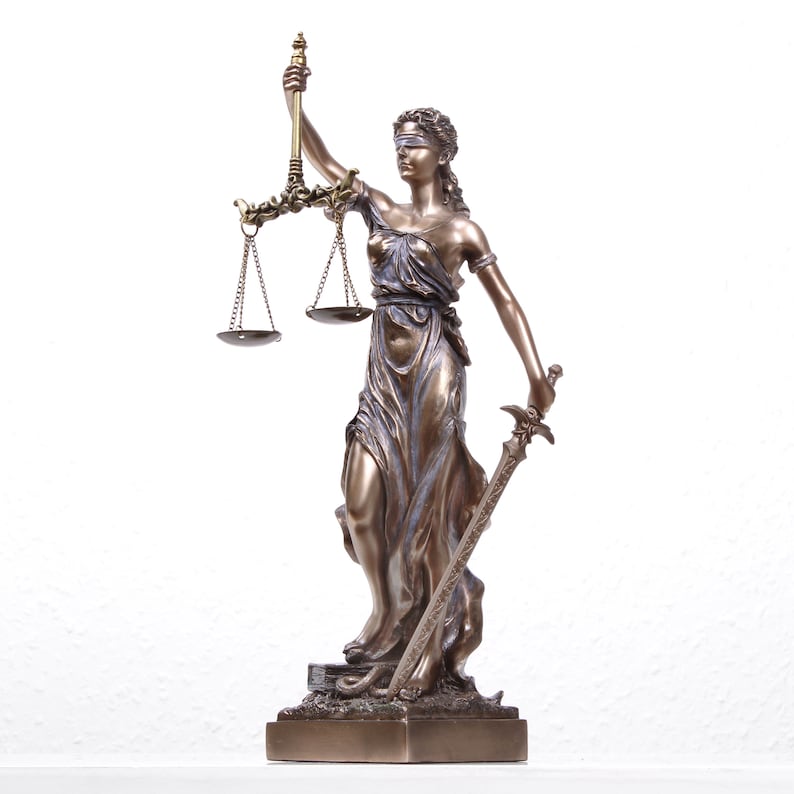 Puede incluir: Una estatua de bronce de la diosa Justicia, una figura femenina con los ojos vendados que sostiene una espada y una balanza de la justicia. La estatua est&aacute; sobre una base rectangular.