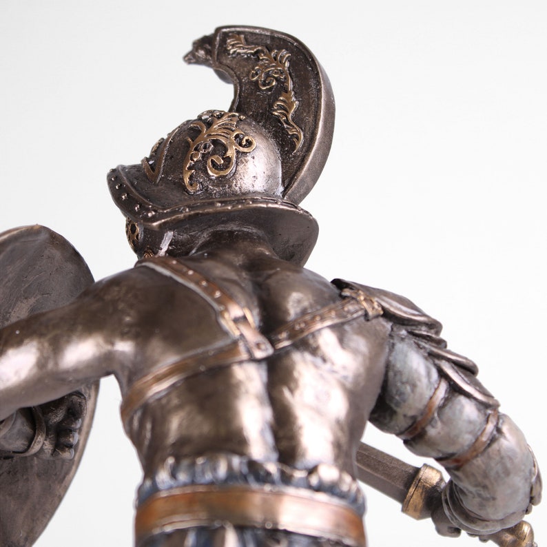 May include: A bronze statue of a gladiator holding a shield and a sword. The gladiator is wearing a helmet with a plume and armor. The statue is detailed and realistic.