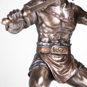 May include: A bronze statue of a gladiator holding a sword. The gladiator is wearing a leather belt with a decorative buckle and a short skirt. The statue is detailed and realistic.