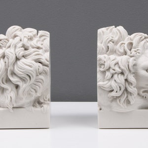 Może przedstawiać: Para białych marmurowych podp&oacute;r do książek w kształcie leżących lw&oacute;w. Lwy mają szczeg&oacute;łowe cechy, w tym grzywy i łapy.