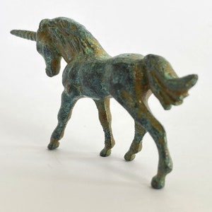 May include: A small, green bronze unicorn figurine with a curled tail and a single horn. The figurine is standing on a white surface.