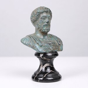 May include: A bronze bust of a man with a beard, on a black marble base. The bust is green and blue, and the man is wearing a toga.