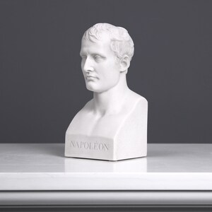 May include: White plaster bust sculpture of Napoleon Bonaparte. The bust is on a white base with the word "NAPOL&Eacute;ON" inscribed on the front.
