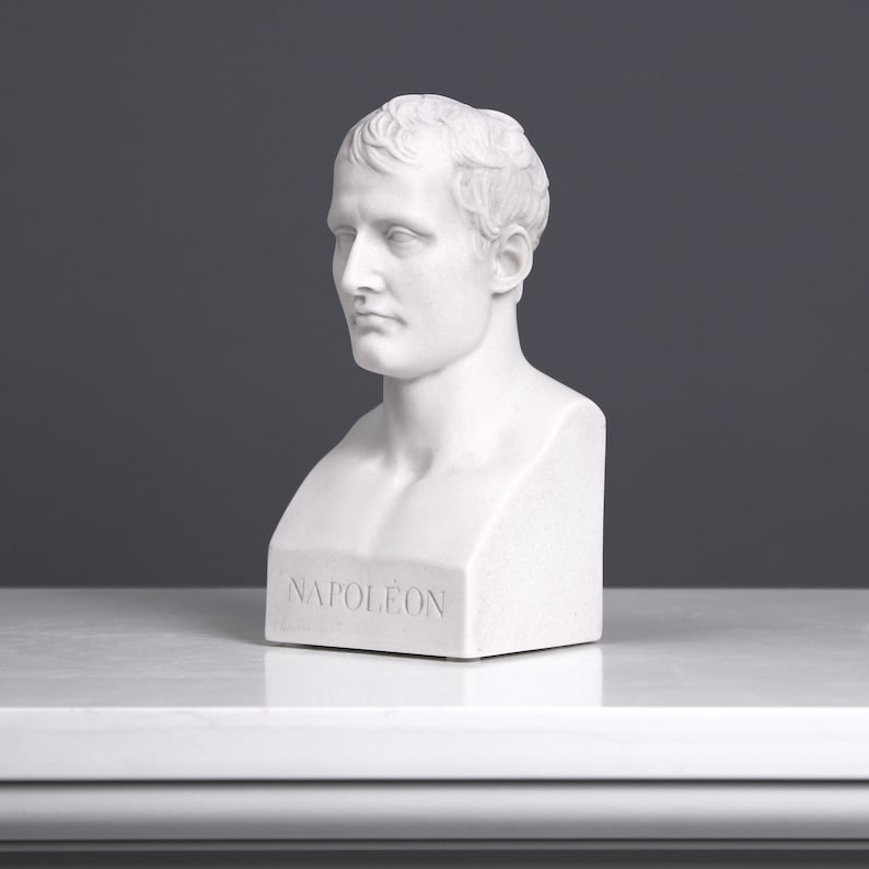 May include: White plaster bust sculpture of Napoleon Bonaparte. The bust is on a white base with the word "NAPOL&Eacute;ON" inscribed on the front.