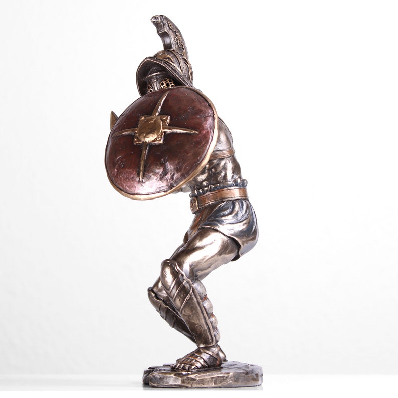 May include: Bronze statue of a gladiator in a fighting pose, holding a shield and sword. The gladiator is wearing armor and a helmet. The statue is on a base.