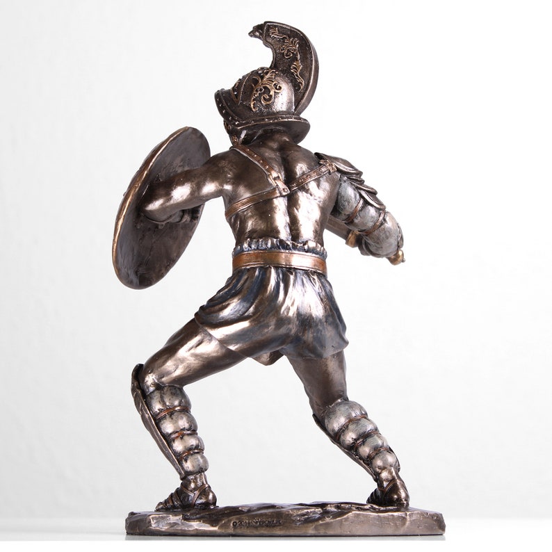 May include: Bronze statue of a gladiator holding a sword and shield. The gladiator is wearing armor and a helmet with a plume. The statue is standing on a base.