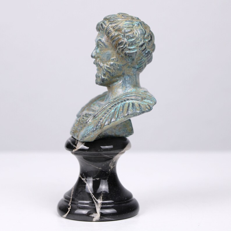 May include: A bronze bust of a man with a beard, on a black marble base. The bust is green and blue, with a patina finish.