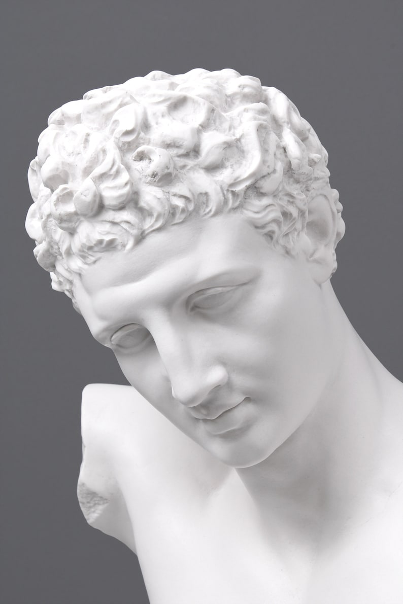 May include: White plaster bust of a person with short, curly hair. The bust is angled down, and the person's face is visible. The person has a serious expression.