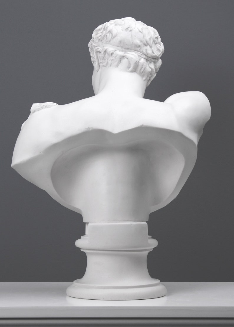 May include: White plaster bust sculpture of a man's torso and head. The bust is on a white pedestal base.