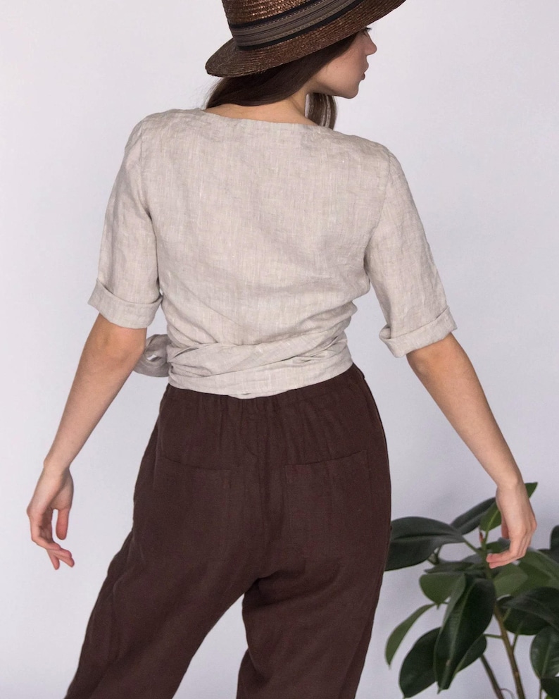 Back view of a natural beige linen wrap blouse with short cuffed sleeves, paired with high-waisted brown linen pants. The blouse ties at the waist for an adjustable fit. Made from 100% breathable linen. Ships quickly from the USA.