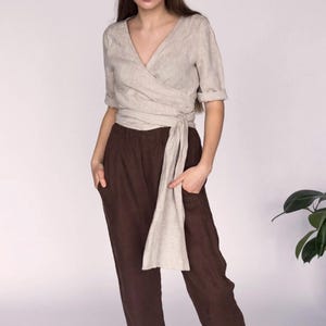 Linen wrap blouse in soft natural beige, featuring a relaxed fit with a long tie waist and hand-finished V-neckline. Styled with wide-leg brown linen pants for a minimalist summer look. Ships from the USA with next-day dispatch.