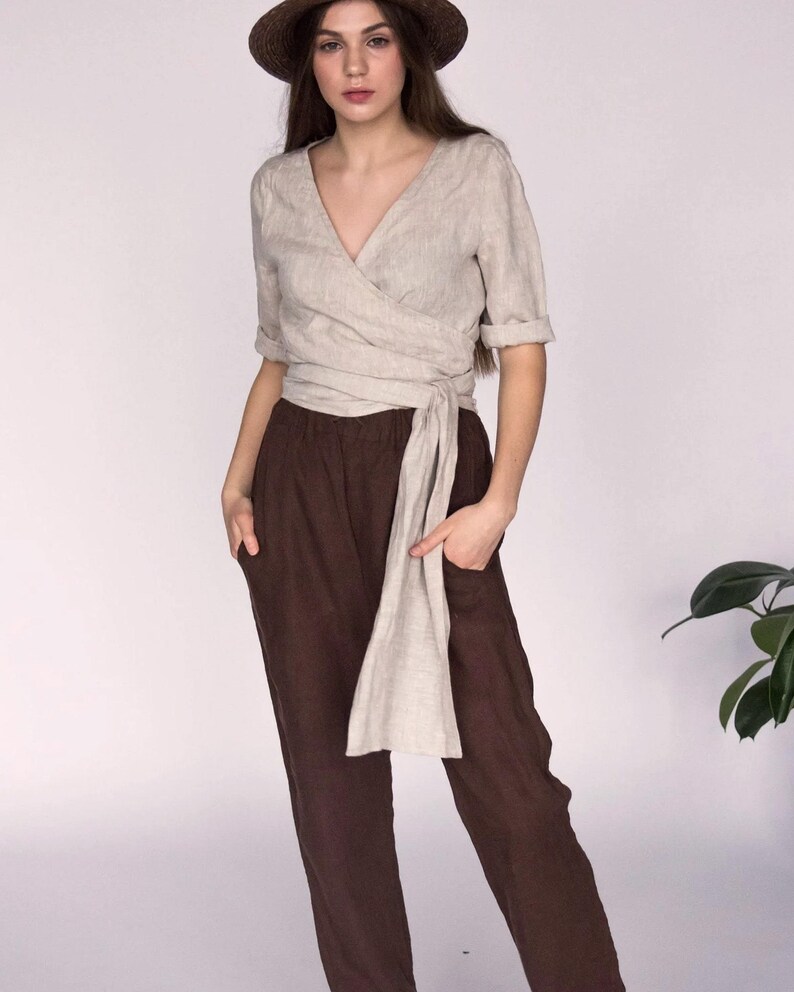 Linen wrap blouse in soft natural beige, featuring a relaxed fit with a long tie waist and hand-finished V-neckline. Styled with wide-leg brown linen pants for a minimalist summer look. Ships from the USA with next-day dispatch.