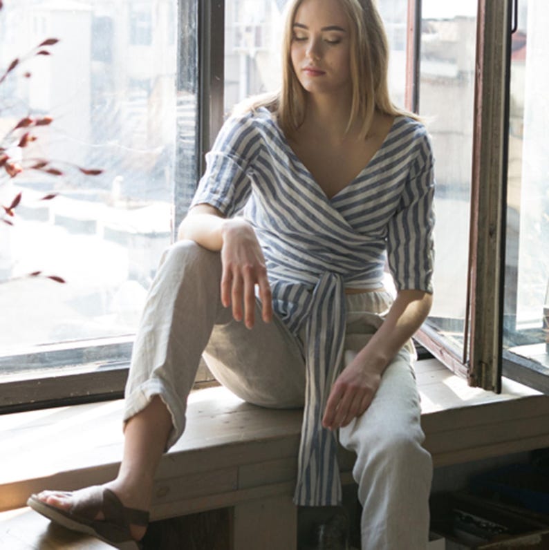 Natural-light photo of a woman in an organic linen wrap top with side tie and V-neckline. A breezy summer blouse handmade from breathable fabric, ideal for warm weather, minimal style, and available in plus sizes for inclusive fit.