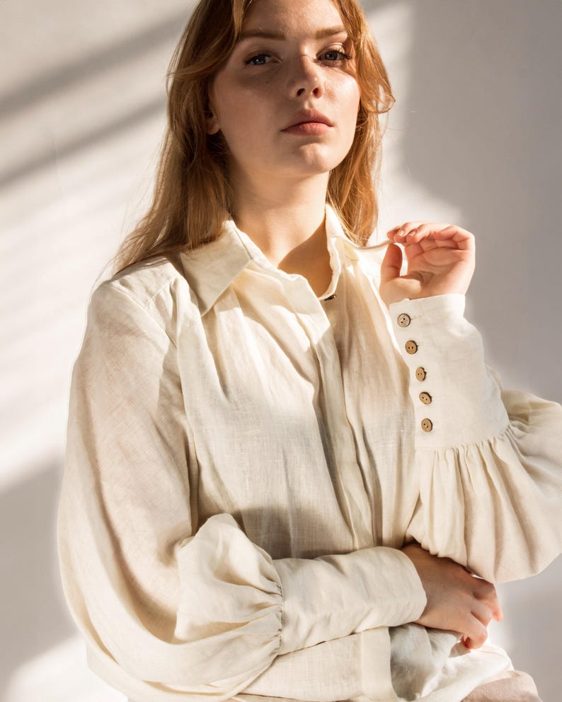 Close-up of romantic white linen blouse with puffed sleeves, vintage-inspired buttoned cuffs, pointed collar, and soft pleats. Feminine Victorian-style shirt perfect for cottagecore fashion, linen office wear, or vintage wardrobe essentials. Made from breathable linen fabric with artisan details. Ships fast from Brooklyn, USA — ready to ship in 24 hours with quick delivery.