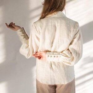 Back view of a white linen blouse with puff sleeves, structured yoke, and vintage-style buttoned cuffs. Features a soft drape and clean seams, showcasing the relaxed fit and craftsmanship. Feminine Victorian-inspired design ideal for cottagecore or slow fashion styling. Ships fast from Brooklyn, USA — ready to ship in 24 hours with quick domestic delivery.
