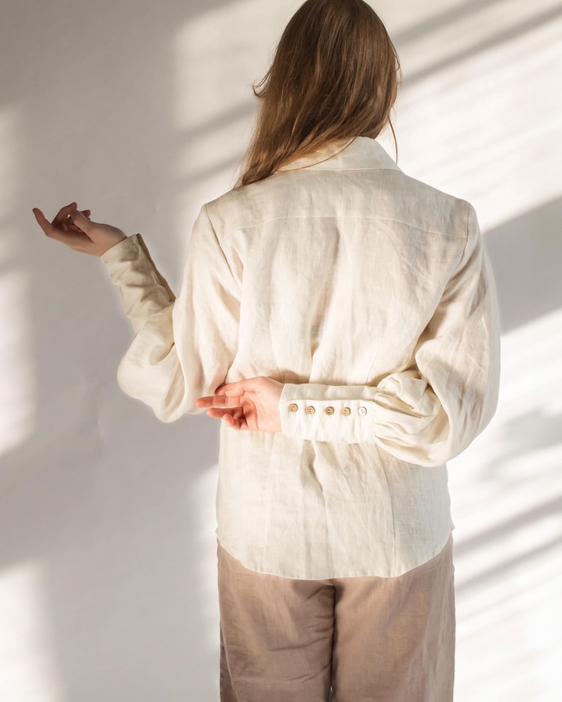 Back view of a white linen blouse with puff sleeves, structured yoke, and vintage-style buttoned cuffs. Features a soft drape and clean seams, showcasing the relaxed fit and craftsmanship. Feminine Victorian-inspired design ideal for cottagecore or slow fashion styling. Ships fast from Brooklyn, USA — ready to ship in 24 hours with quick domestic delivery.