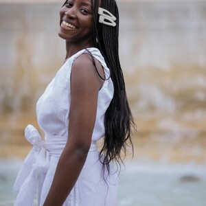 Smiling woman in a white linen wrap dress with a feminine bow-tie waist, photographed from the side. The dress features a V-back, wide straps, and a flattering silhouette made of breathable natural linen. Perfect for summer vacations, beach dinners, honeymoons, or minimalist weddings. A joyful, romantic look ideal for confident women who value comfort and elegance. Ships fast from the USA within 1 business day.