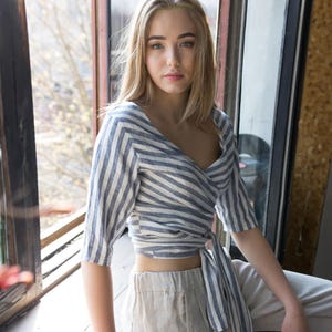 Model styled in a lightweight striped linen wrap blouse with a soft tie waist, cropped length, and relaxed 3/4 sleeves. An elegant organic summer top designed for everyday comfort and cottagecore-inspired outfits is also offered in plus size options.
