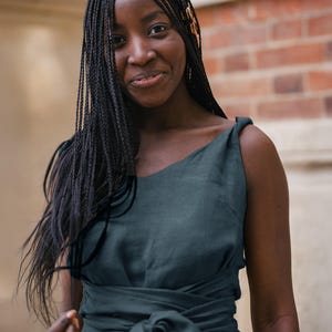 Ready to ship in 1 day, this sleeveless linen midi dress in soft green features a unique asymmetric neckline and wide tie belt for a flattering silhouette. Perfect for women who love natural fabrics and timeless summer looks, it’s ideal for vacations, casual outings, or effortless everyday style.
