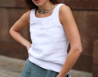 May include: A white linen tank top with a square neckline and a teal skirt. The top is sleeveless and has a relaxed fit. A silver necklace is worn around the neck. The outfit is casual and stylish.
