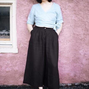 Ready to ship from USA in 24 hours — black linen culottes for women with wide leg design, deep pockets, and flattering high waist with pleats. Styled with a blue wrap top for a minimalist, relaxed look. Breathable and soft, perfect for summer, travel, or capsule wardrobe. Comfortable fit with elastic back waist, great for plus size, coastal, or modern cottagecore style.