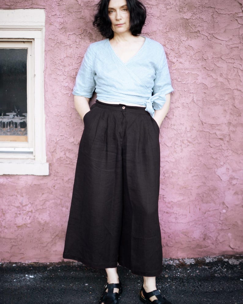 Ready to ship from USA in 24 hours — black linen culottes for women with wide leg design, deep pockets, and flattering high waist with pleats. Styled with a blue wrap top for a minimalist, relaxed look. Breathable and soft, perfect for summer, travel, or capsule wardrobe. Comfortable fit with elastic back waist, great for plus size, coastal, or modern cottagecore style.