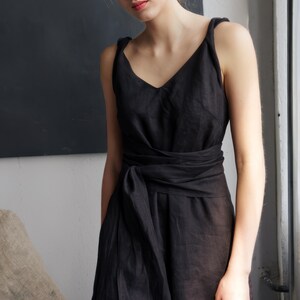 Ready to ship in 1 day, this elegant black linen dress features a soft V-neckline, twisted straps, and a wide waist tie that accentuates the silhouette. A timeless midi-length piece ideal for summer events, travel, or casual evenings, offering both comfort and sophistication for modern women.