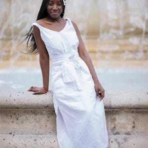 White linen midi dress with V-neckline front and back, flattering for all body types. Twisted straps and sewn-in waist tie create a beautiful silhouette. High side slits and side seam pockets add comfort and ease. Made from breathable linen—ideal for summer vacations, casual weddings, and romantic dinners. A feminine style for women who value elegance and ease. Ships fast from the USA within 1 business day.