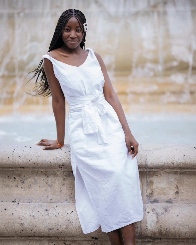 White linen midi dress with V-neckline front and back, flattering for all body types. Twisted straps and sewn-in waist tie create a beautiful silhouette. High side slits and side seam pockets add comfort and ease. Made from breathable linen—ideal for summer vacations, casual weddings, and romantic dinners. A feminine style for women who value elegance and ease. Ships fast from the USA within 1 business day.