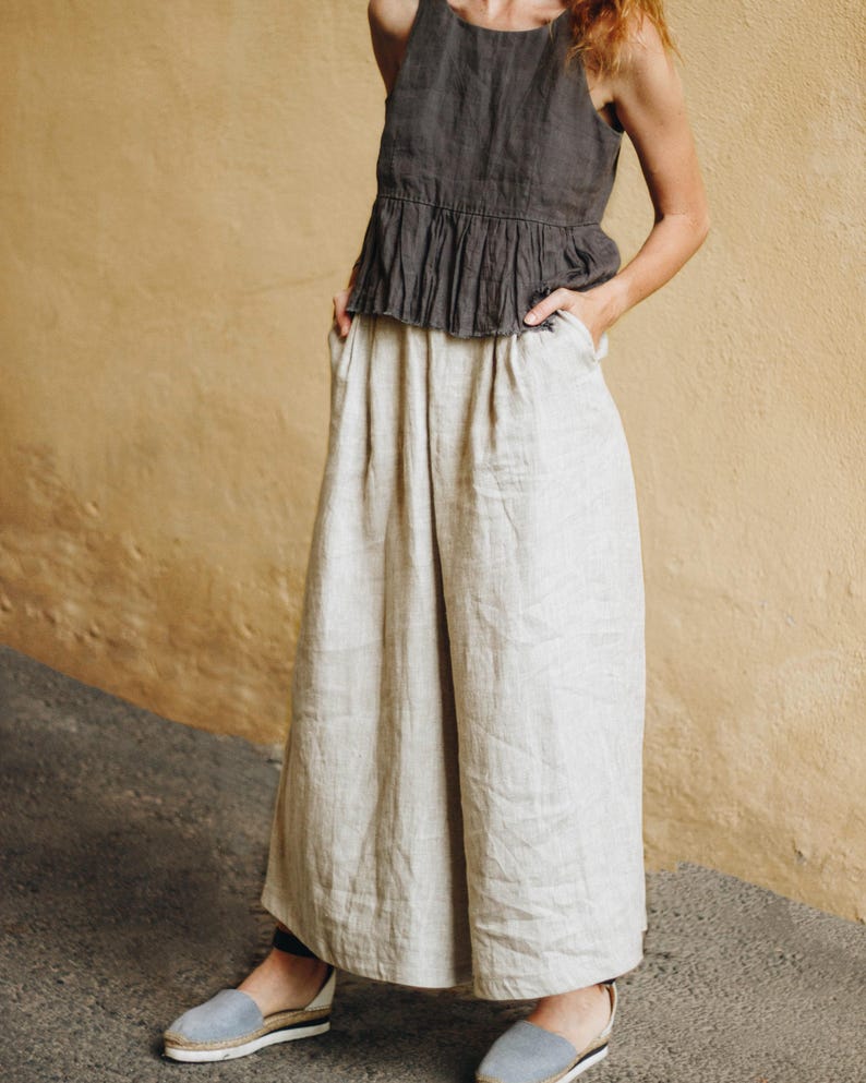 These natural undyed linen culottes for women feature a high-waisted fit with an elastic back, wide legs, and deep pockets. Made from breathable, sustainable fabric, they offer a flowy and flattering silhouette with soft pleats for comfort and movement. Perfect for a capsule wardrobe, plus-size inclusive, and ideal for summer travel, lounging, or cottagecore looks. Ready to ship in 24 hours from the USA with fast delivery nationwide.