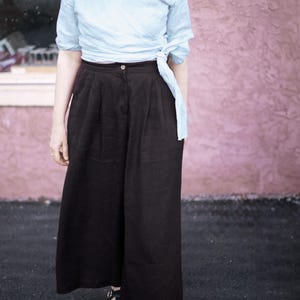 Black linen culottes for women styled with a soft wrap top, featuring wide leg silhouette, flattering pleats, and deep pockets. High waisted fit with elastic back for comfort and movement. Lightweight and breathable for summer travel, casual outings, or minimalist capsule wardrobe. Effortless and chic, plus size inclusive. Ready to ship in 24 hours from USA with fast delivery across the US.