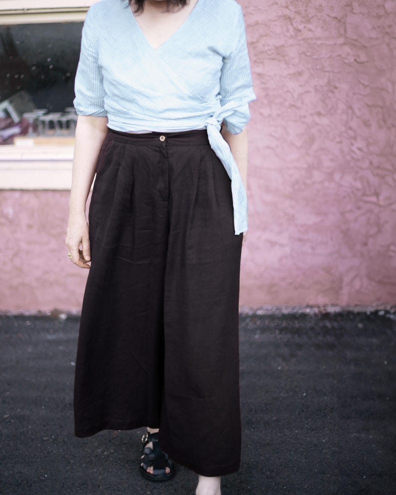 Black linen culottes for women styled with a soft wrap top, featuring wide leg silhouette, flattering pleats, and deep pockets. High waisted fit with elastic back for comfort and movement. Lightweight and breathable for summer travel, casual outings, or minimalist capsule wardrobe. Effortless and chic, plus size inclusive. Ready to ship in 24 hours from USA with fast delivery across the US.