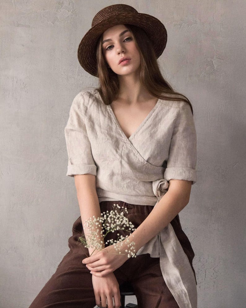 Linen wrap blouse for women made from softened natural linen, featuring a V-neckline with delicate hand stitching along the edge, a tie waist, and minimalist silhouette. Ideal for a creative summer wardrobe, city travel, or vacation styling. Ships quickly from the USA, dispatched within 1 day.