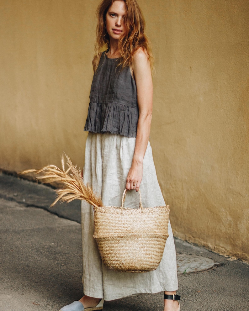 Natural linen wide leg culottes styled with a sleeveless dark top and straw bag. Relaxed fit, high waist with adjustable back, deep pockets, and flowy cropped silhouette. Perfect for plus size, beachy, boho or coastal grandma style. Breathable and comfy travel pants for summer, lounging, or vacation. Ready to ship in 24 hours from USA with fast delivery across the US.