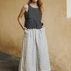 High-waisted wide leg linen culottes in natural undyed color, styled with a dark sleeveless peplum top. Featuring deep side pockets, soft front pleats, and an adjustable elastic waistband at the back for a flexible fit. Made from breathable, sustainable fabric for comfort and movement. A versatile piece for minimalist, resort, or cottagecore looks. Ready to ship in 24 hours from USA with fast delivery across the country.