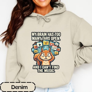 May include: A beige hooded sweatshirt featuring a graphic of a squirrel holding its head with both hands. Above and below the squirrel, the text reads: MY BRAIN HAS TOO MANY TABS OPEN. AND I CAN'T FIND THE MUSIC. The graphic includes browser tabs.