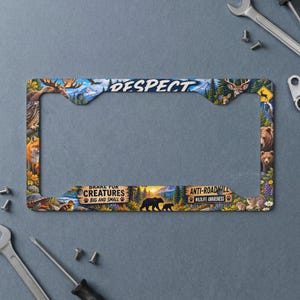 May include: A rectangular license plate frame featuring a forest landscape with various wildlife including a bear, deer, and fox. The top text reads "RESPECT" and the bottom text reads "BRAKE FOR CREATURES BIG AND SMALL" and "ANTI-ROADKILL WILDLIFE AWARENESS".