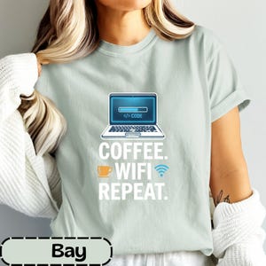 Könnte beinhalten: Ein helles salbeigrünes T-Shirt mit einer Laptop-Grafik, die einen Ladebalken und den Text "</> CODE" zeigt. Darunter steht in weißer Schrift "COFFEE. WIFI REPEAT.", ergänzt durch ein kleines orangefarbenes Kaffeetassen-Symbol und ein blaues WLAN-Symbol.