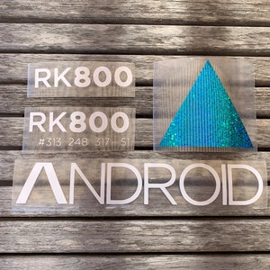 May include: Three white vinyl stickers with the text "RK800" and "ANDROID". The sticker with the text "RK800" also includes the numbers "#313 248 317 - 51". A blue glitter triangle sticker is also included.